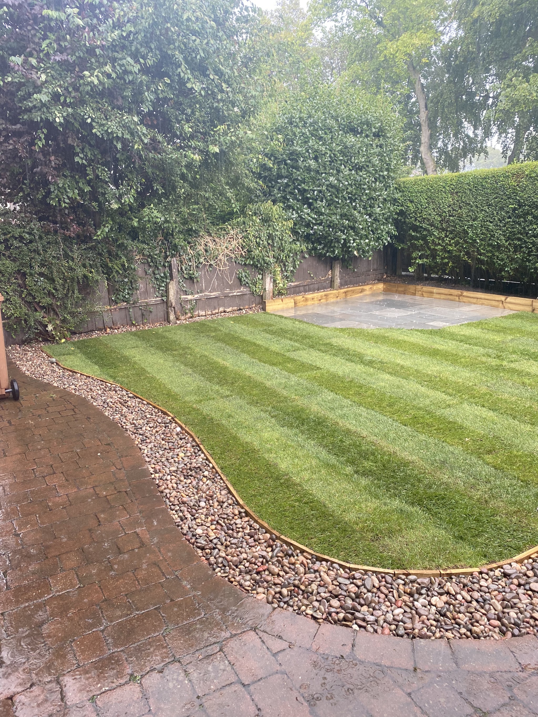A striped lawn with a brick path and a curved pebble border