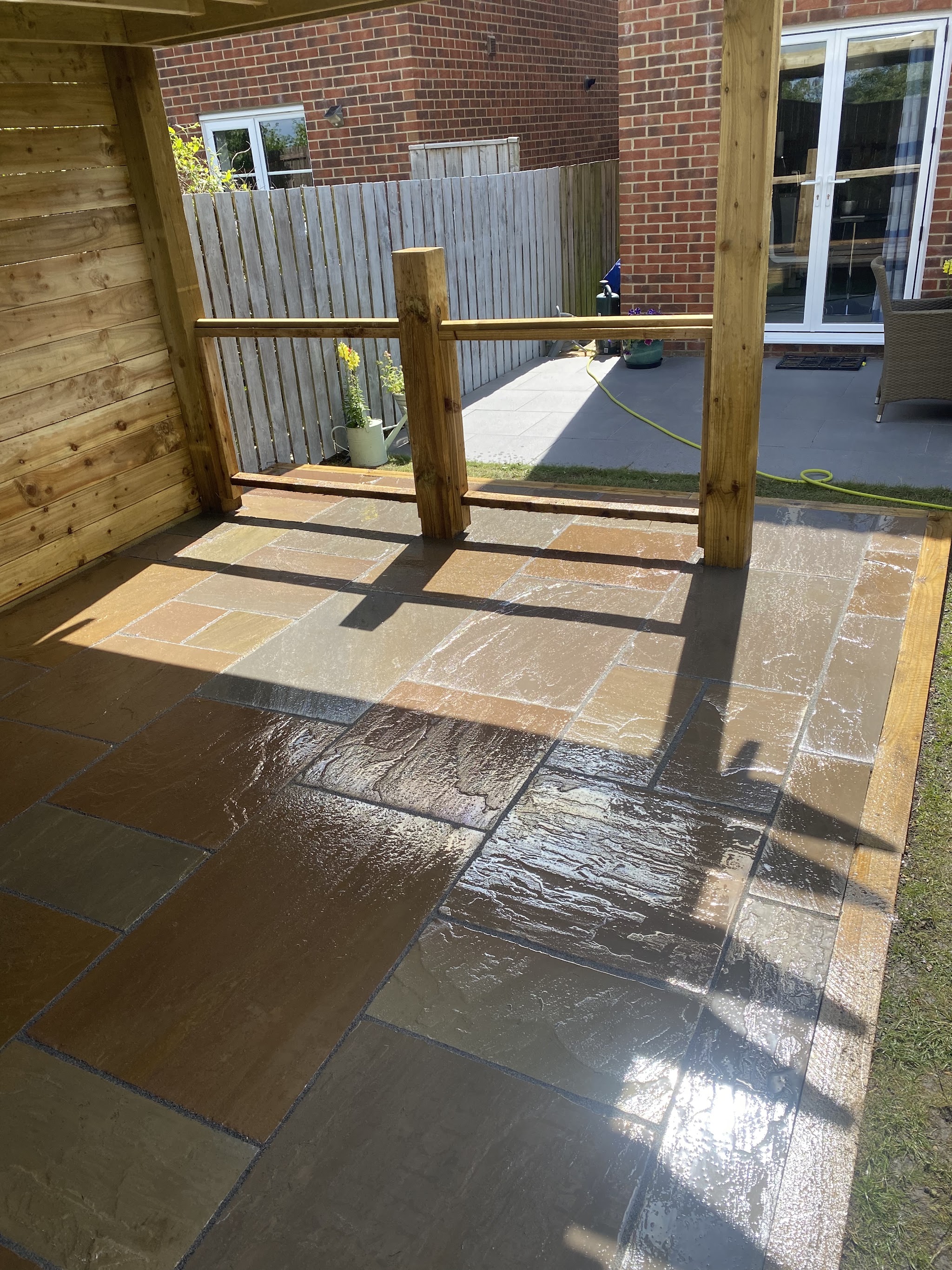 A sandstone patio under a timber pergola beside a slatted screen