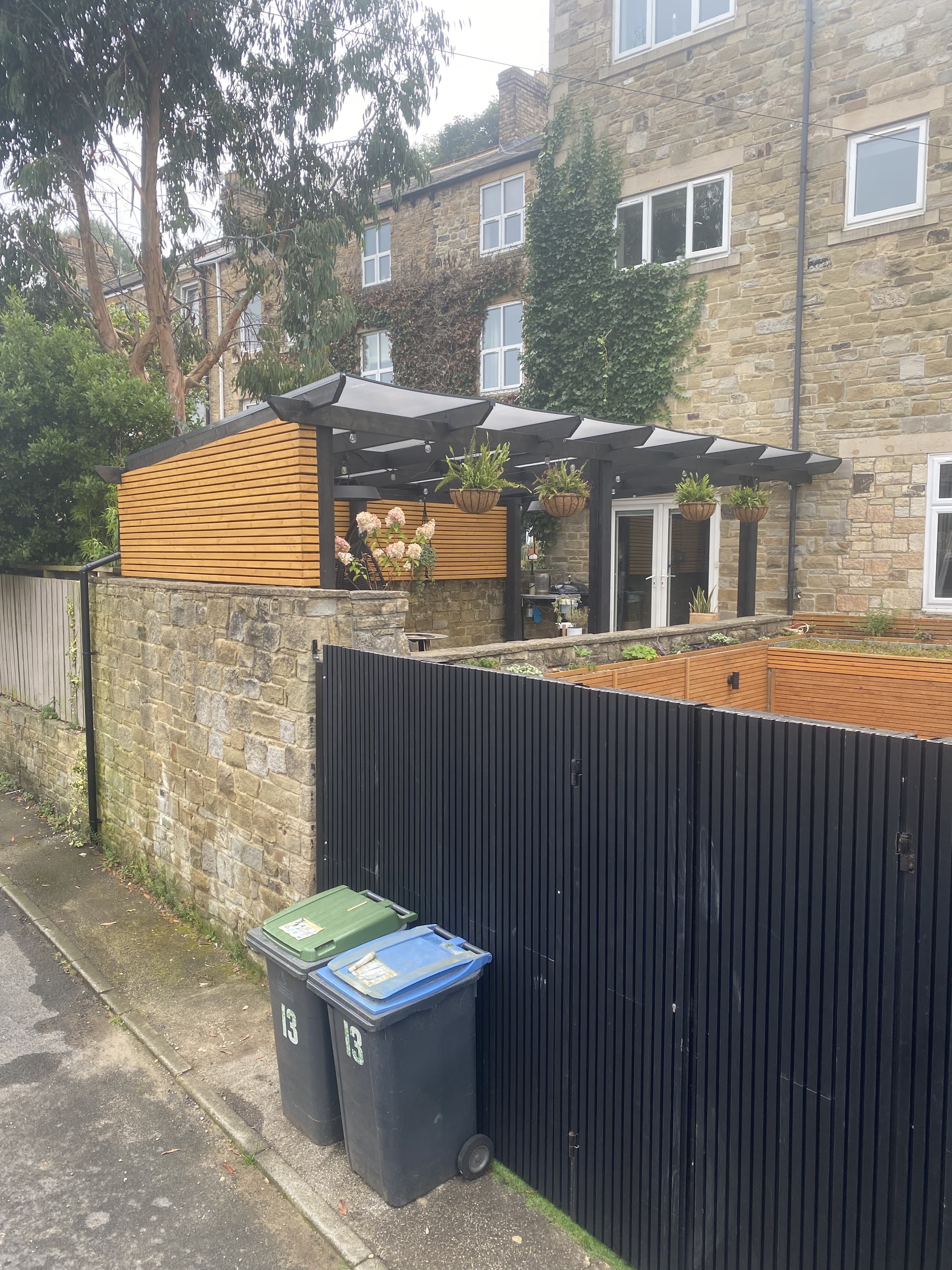 A steel-framed canopy over a slatted timber screen beside black fencing