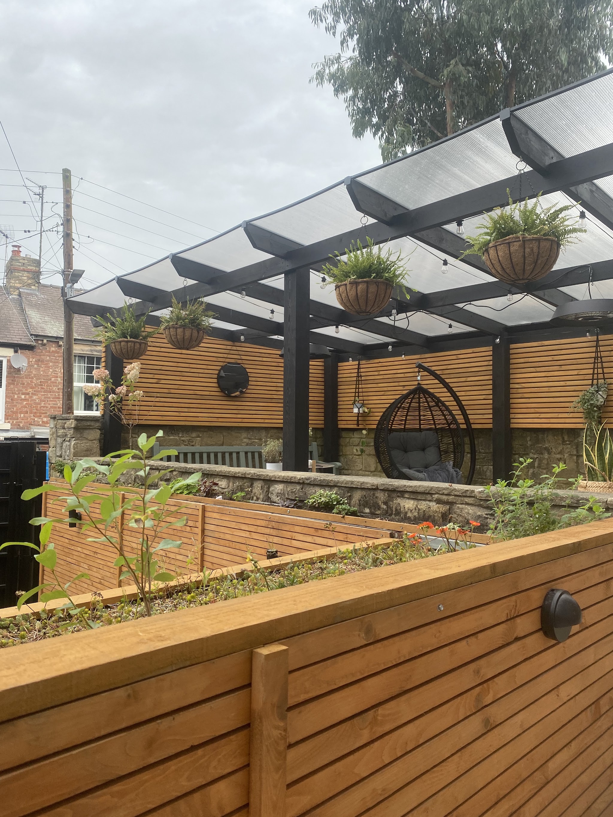 A canopy with hanging baskets above a slatted raised planter