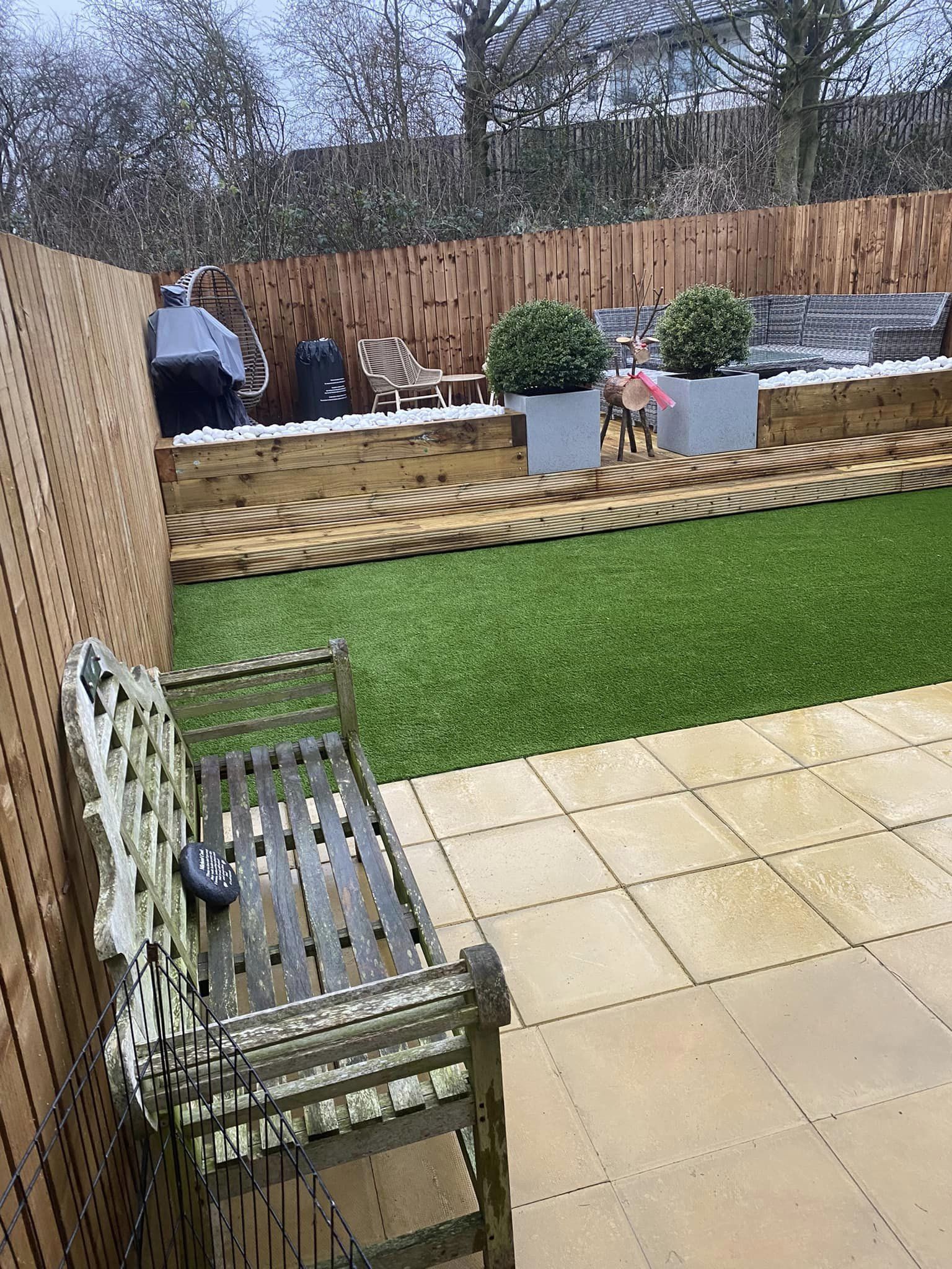 A garden with an artificial lawn, raised sleeper beds and a sandstone patio