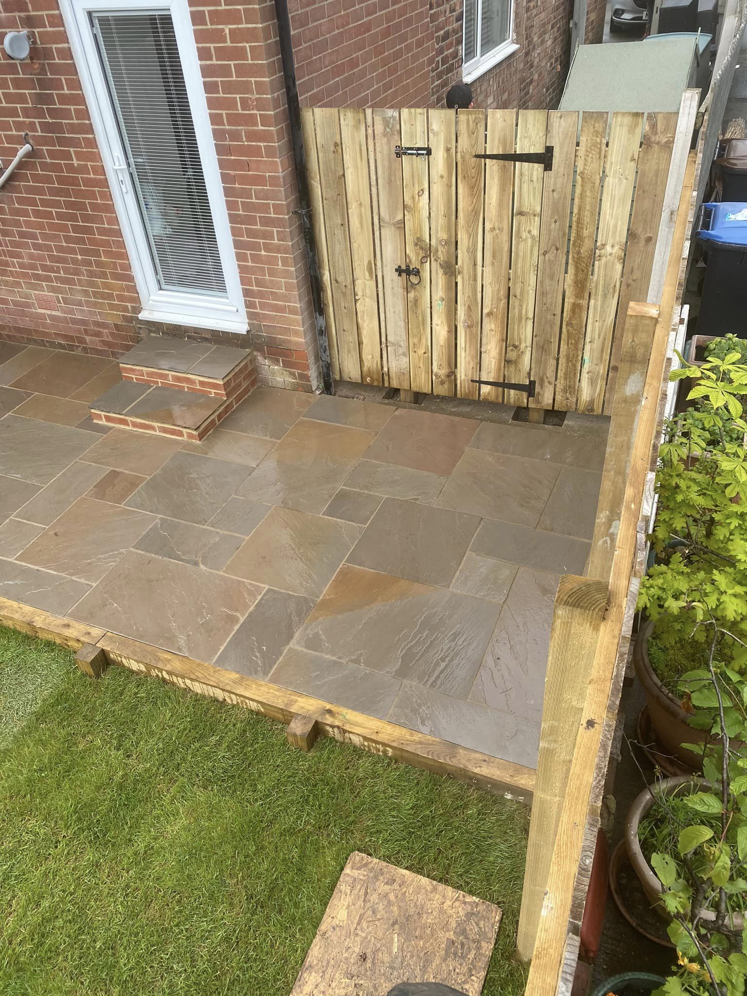 A flagged patio with steps up to a timber gate and a new fence beside a brick house